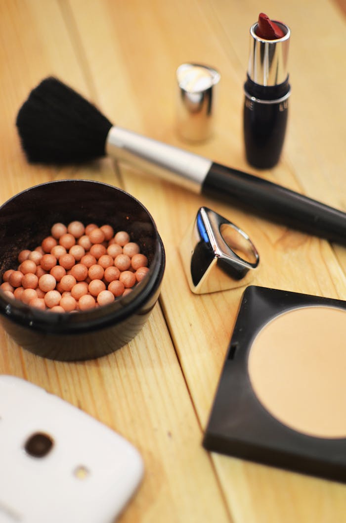 A stylish collection of makeup items arranged on a wooden table, including lipstick and brush.